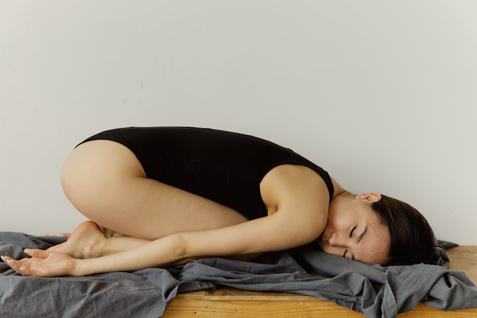 body scan meditation - An Asian woman in a black bodysuit is resting peacefully on a gray blanket against a white wall.