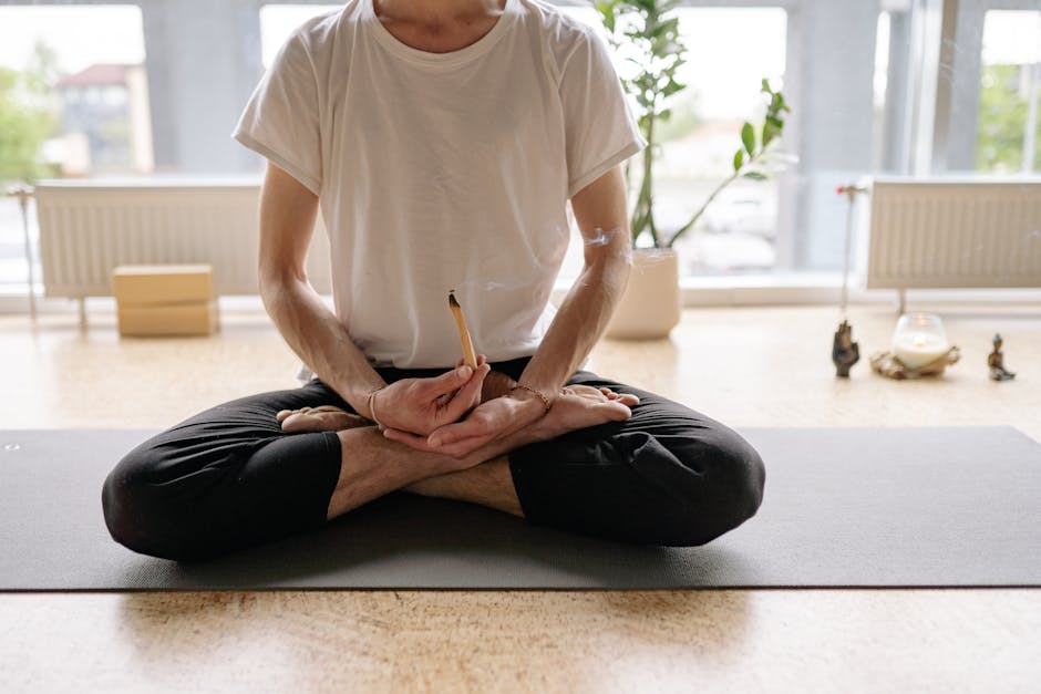 mantra meditation - A man sits cross-legged holding an incense stick during yoga meditation indoors.