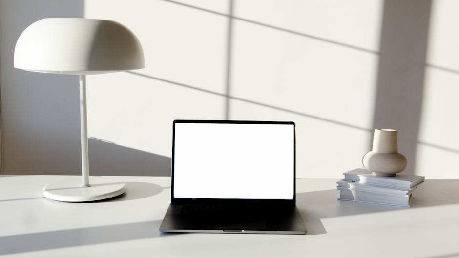 monotasking - Sleek office desk setup featuring laptop, modern lamp, and decorative vase in soft lighting.