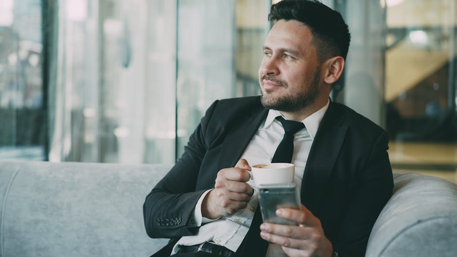 mindful leadership - A man in a suit relaxing with a coffee while using a smartphone indoors.