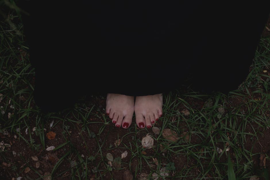 walking meditation - Close-up of bare feet wrapped in a dark cloak standing on grass, evoking mystery.