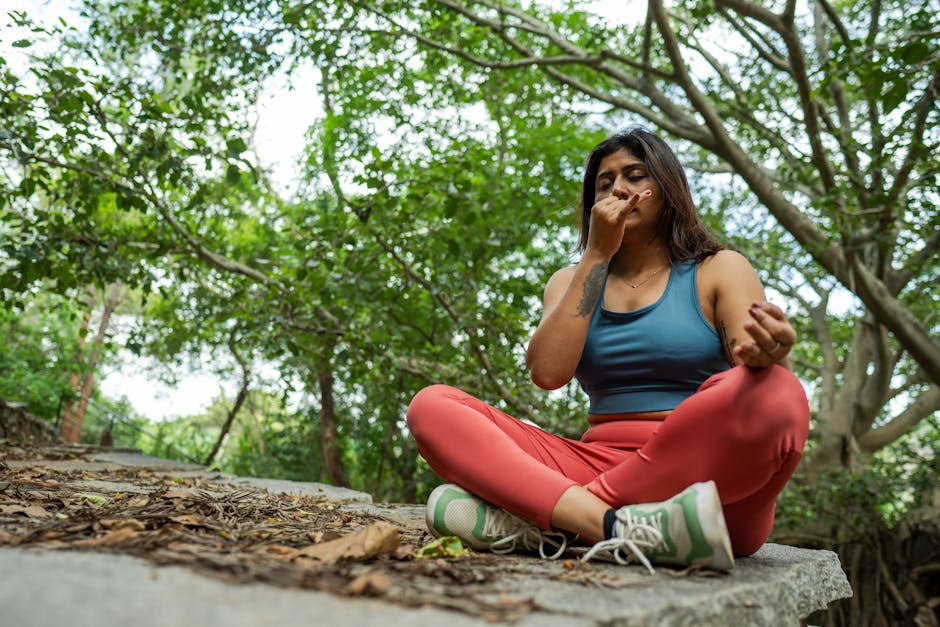 mindfulness news May 2026 - Young woman meditating in a forest, practicing yoga breathing exercises on a stone platform.