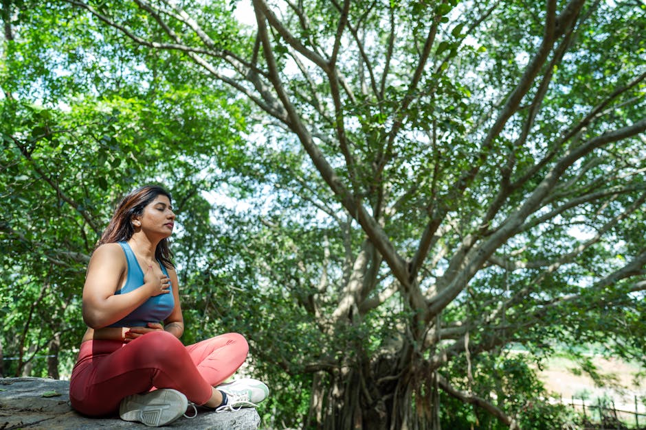 weekly mindfulness news - A woman meditates in a serene outdoor setting, surrounded by lush greenery.