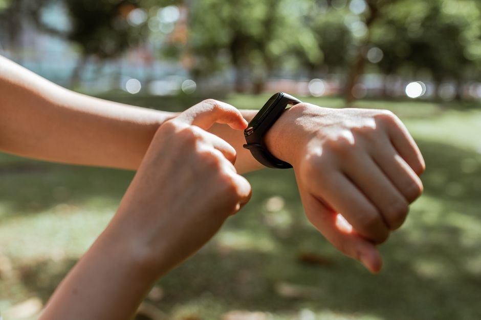 mindfulness and mental wellness - Crop faceless slim female tapping on fitness bracelet screen while training time in sunny summer park