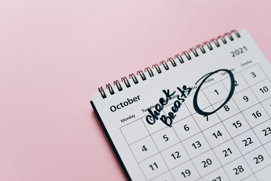 fitness accountability app - October calendar with breast check reminder, emphasizing health awareness on a pink background.