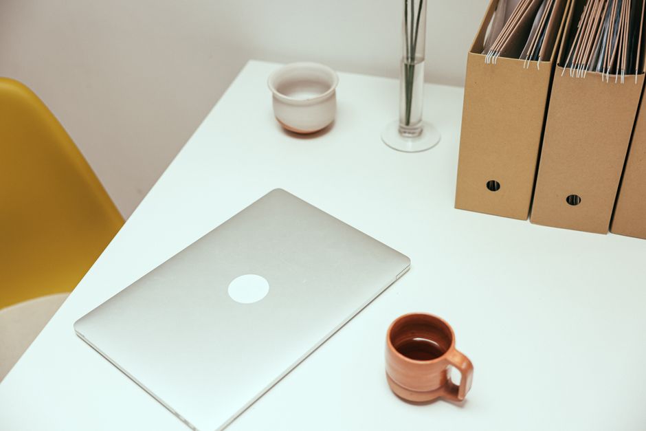 habit friction reduction - A minimalist home office desk setup with laptop, coffee cup, and file organizers.