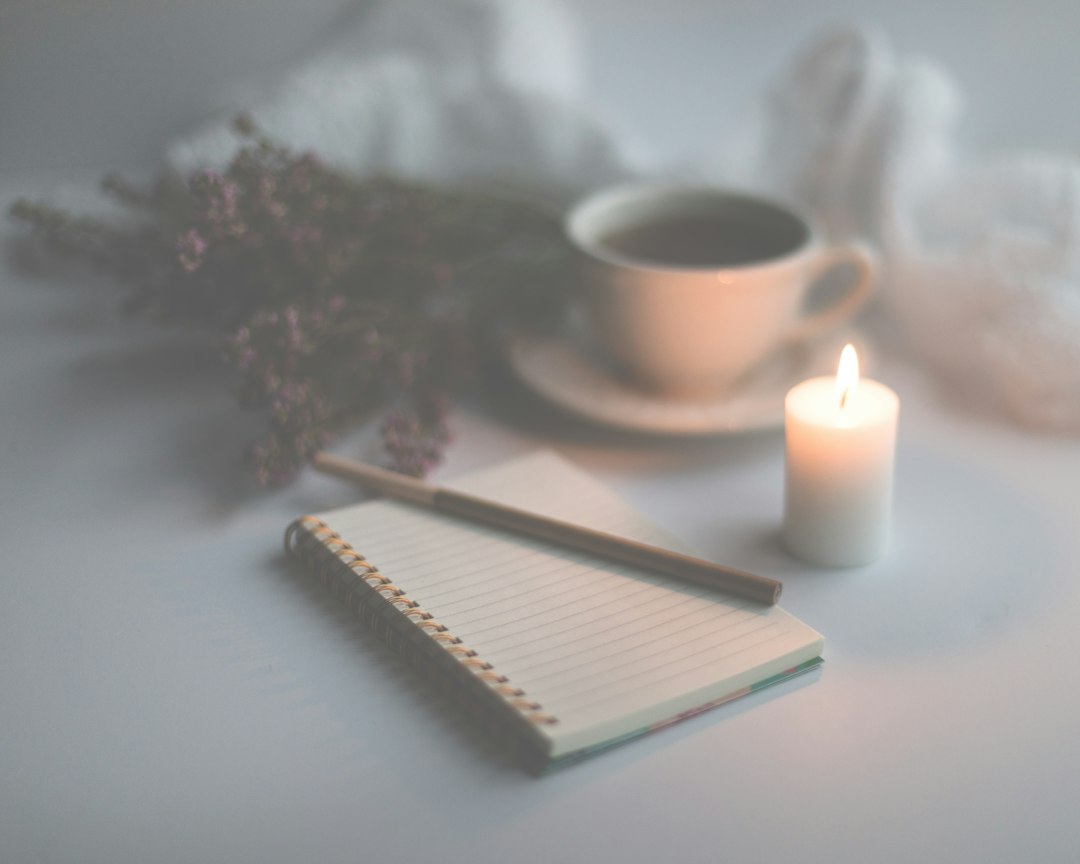 mental wellness news - white candle on white ruled paper beside white ceramic mug