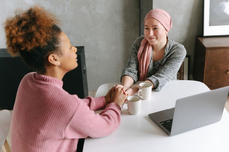 mental wellness news - Two women sharing a supportive conversation over coffee indoors. One woman wears a head wrap.